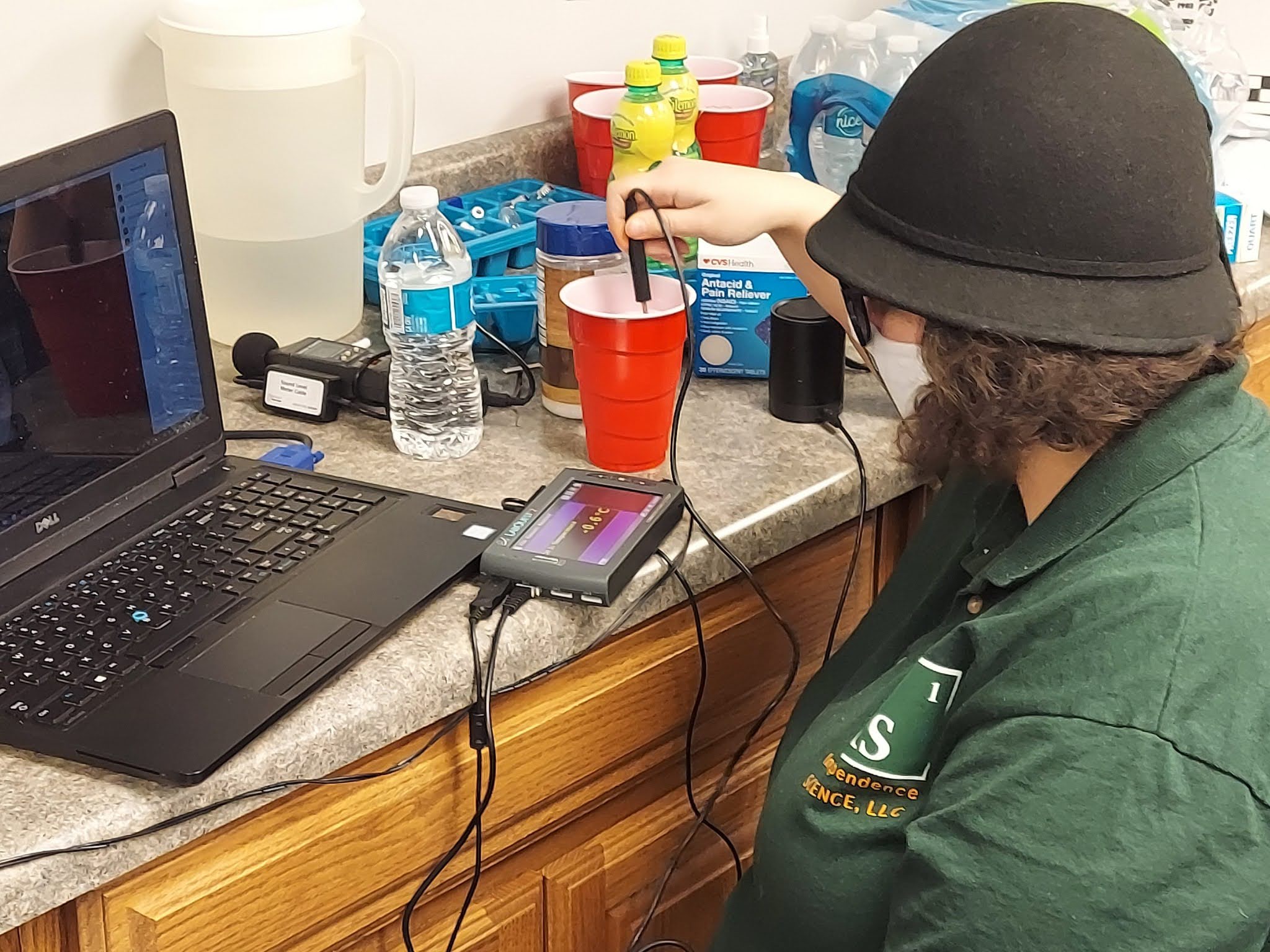 Ashley stirs a cup of salted ice water with a temperature probe and the Talking LabQuest for a virtual demo wearing a matching Independence Science shirt and face mask